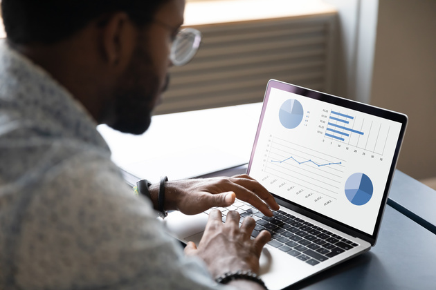 A man sits at a desk analyzing data on a laptop. 